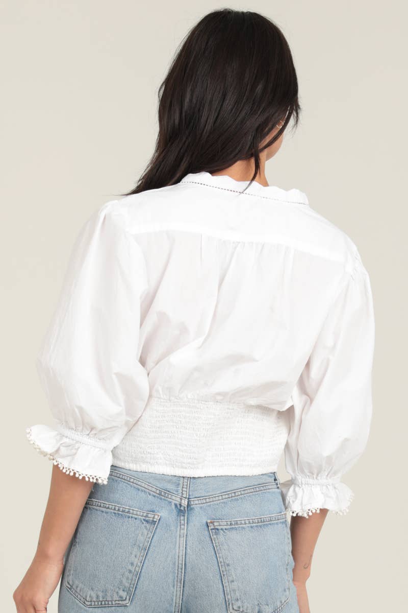 White eyelet embroidered blouse with button front, puffed sleeves, smocked cuffs, and a fitted smocked waist, shown from the .