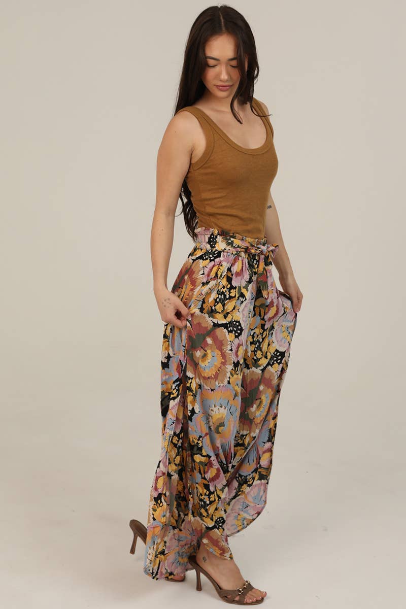 Woman facing side wearing a brown tank top and Angie colorful floral pants on a beige background