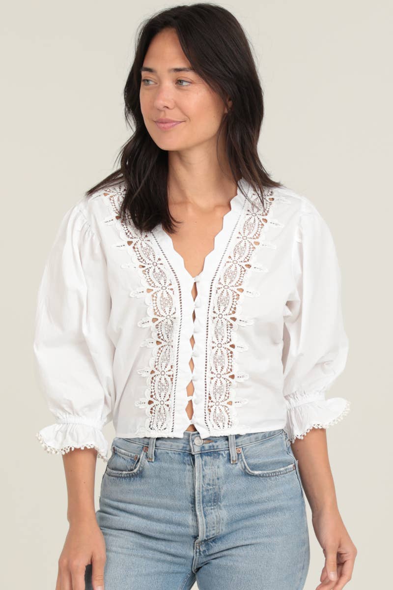 White eyelet embroidered blouse with lace trim, button front, puffed three-quarter sleeves, and scalloped cuffs, worn with.