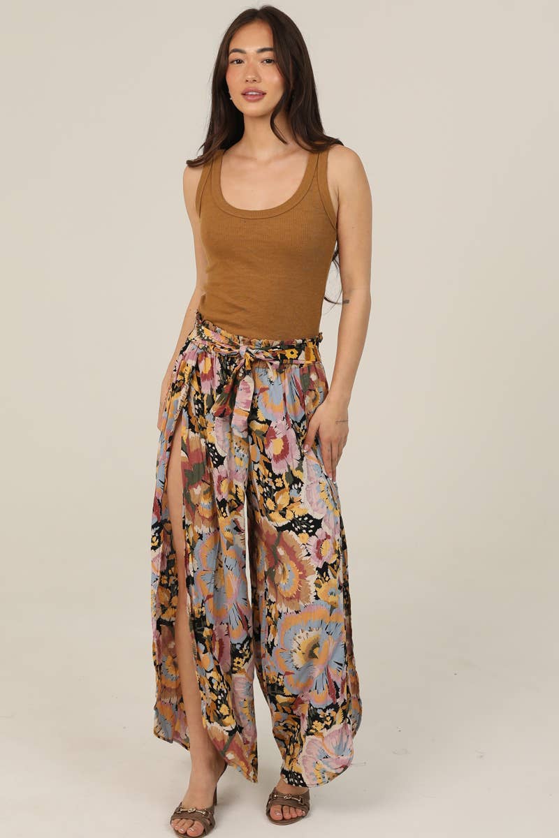 Woman facing forward wearing a brown tank top and Angie colorful floral pants on a beige background