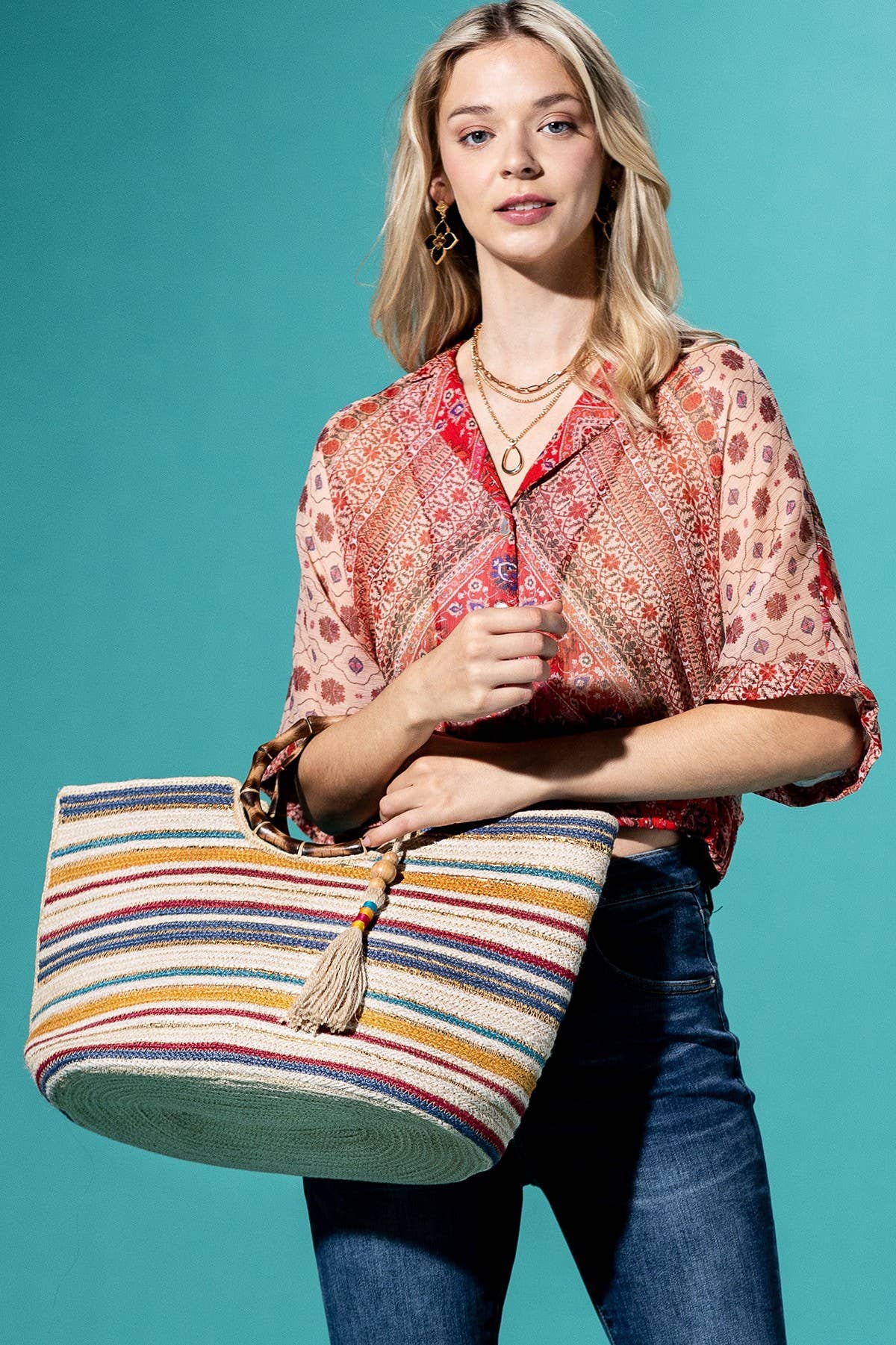 Striped bamboo jute tote bag with multicolored horizontal bands and bamboo handle held by woman in patterned blouse and.